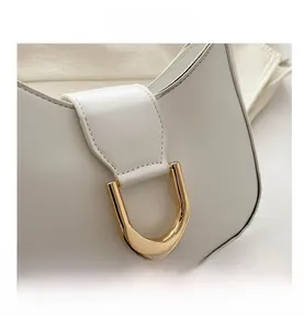 Detail of white leather dumpling bag featuring a polished gold U-shaped hardware clasp