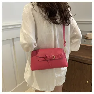 Détail du sac bandoulière rose fuchsia avec nœud doré porté sur une chemise blanche