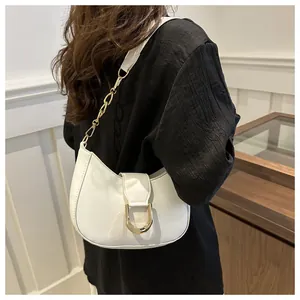 Detail of white half-moon shoulder bag with golden U-shaped buckle on a model