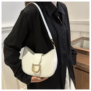 Detail of minimalist white crescent bag with gold horseshoe buckle on model arm