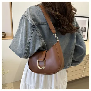 Detail of a brown crescent shoulder bag featuring a gold U-shaped metal clasp and stitching