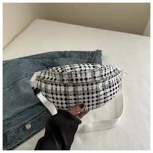 Detail of minimalist houndstooth waist bag with white strap on a denim jacket background