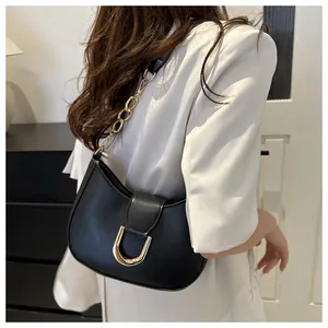 Detail of a black dumpling shoulder bag featuring a gold U-shaped buckle and chain strap