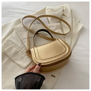 Dettaglio della borsa a sella dorata con cuciture ad arco su blazer bianco e rivista