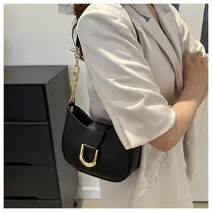 Detail of minimalist black underarm bag with gold horseshoe buckle and chain strap