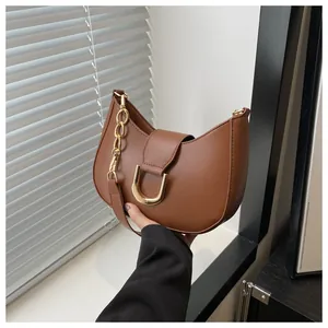 Detail of caramel leather croissant bag featuring a gold U-shaped buckle and chunky chain