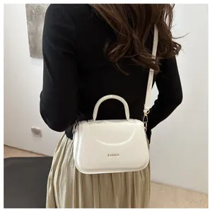Dettaglio di una borsa a tracolla in pelle bianca con scritta FASHION indossata da una modella