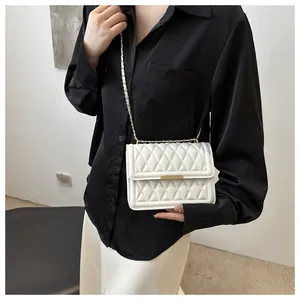Detail of white quilted crossbody bag with gold chain strap and metallic clasp on a model