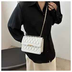 Detail view of quilted white faux leather shoulder bag with gold chain strap worn by model