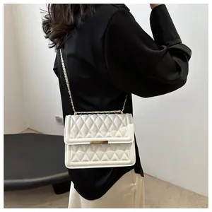 Detailed view of white quilted crossbody bag with gold chain strap on model's shoulder