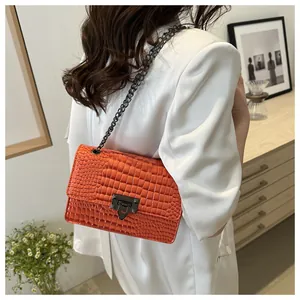 Détail du sac bandoulière orange en cuir gaufré avec chaîne en métal sur blazer blanc
