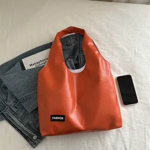 Large orange oil wax leather tote bag for women with fashion label on white bedding
