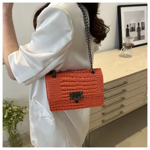 Détail d'un sac bandoulière orange à motif crocodile avec chaîne métallique et fermoir rotatif
