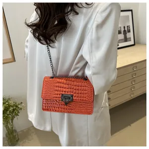 Détail d'un petit sac carré orange vif avec bandoulière chaîne et texture crocodile