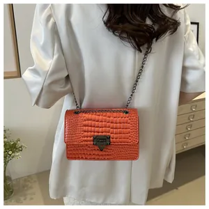 Sac à main orange effet croco avec fermoir noir porté sur un blazer blanc chic