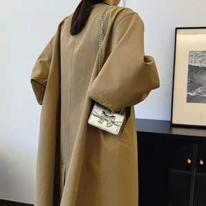 Mini silver chain crossbody bag with bow detail worn over a khaki trench coat
