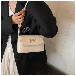 Macro shot of off-white leather shoulder bag with a silver metal bow detail and knot strap