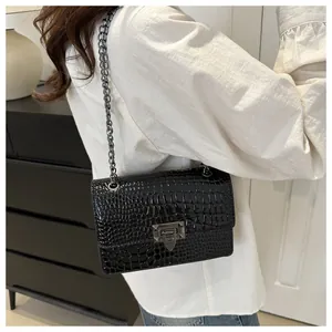 Détail d'un sac noir à texture pierre avec chaîne et fermoir porté à l'épaule par un modèle