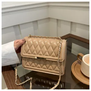 Close-up of beige quilted crossbody bag with gold chain strap and metal clasp on a table