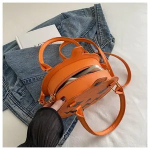 Top view of pumpkin-shaped orange PU leather handbag on white bed with denim jacket