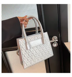 Détail du sac à main argenté avec texture géométrique et poignées cylindriques