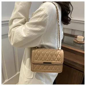 Detail of beige quilted crossbody bag with metal clasp and gold chain on model