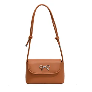 Brown leather crossbody bag with a silver metal bow buckle and knotted shoulder strap