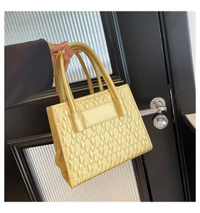 Détail du sac à main doré avec texture gaufrée 3D et doubles poignées cylindriques
