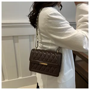 Close-up of a quilted dark brown crossbody bag with gold lock and chain strap on a model