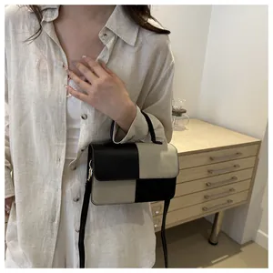 Dettaglio di una borsa a tracolla bicolore con manico superiore e eleganti ganci in metallo