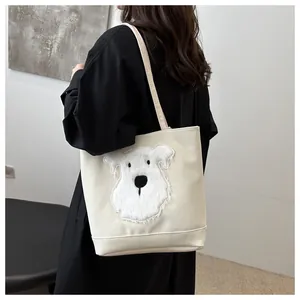 Detail of a creamy white tote bag with a cute embroidered puppy and slim shoulder straps