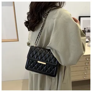 Detail of black quilted leather crossbody bag with gold buckle and chain strap on model