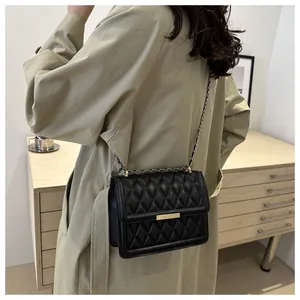 Fashionable black quilted crossbody bag with a gold clasp worn over a beige trench coat