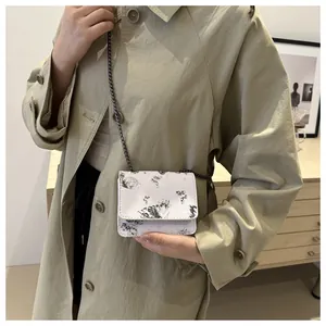 Détail du sac bandoulière blanc imprimé papillon avec chaîne en métal sur mannequin en trench
