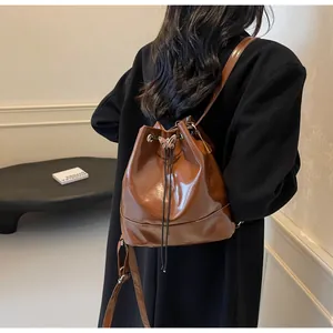 Detail of a brown glossy PU leather bucket bag with silver butterfly buckle on a model