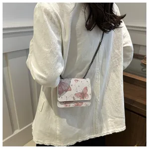 Détail d'un petit sac blanc imprimé papillon avec bandoulière chaîne sur femme