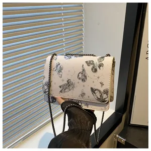 Détail d'un sac bandoulière chic avec imprimé papillon et chaîne en métal gris