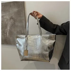 Detail of silver crocodile-embossed tote bag with golden metal tag and shoulder straps