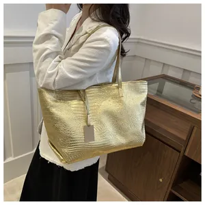 Detailed view of crocodile pattern gold tote bag with H logo on model with white blazer