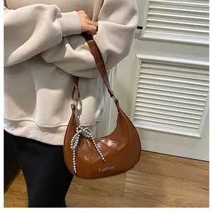 Detail of dark brown glossy crescent bag with an elegant pearl bow pendant and white logo