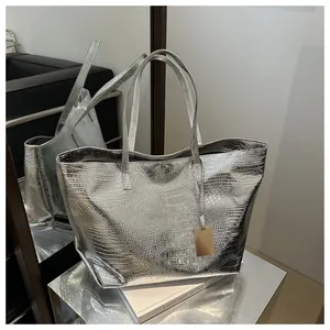 Detailed close-up of silver crocodile embossed tote bag with gold metal charm and straps