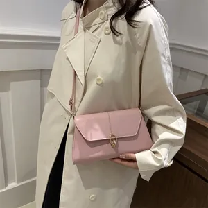 Sac sous le bras en cuir rose avec fermoir doré porté avec un trench-coat beige