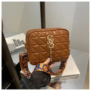 Close-up of brown quilted bag with gold S-logo and graffiti patterned wide shoulder strap