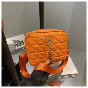 Close-up of bright orange quilted crossbody bag with gold S-buckle and logo strap