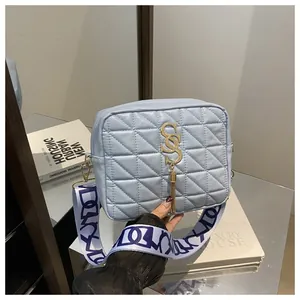 Detail view of quilted light blue crossbody bag with gold metal S logo and tassel charm
