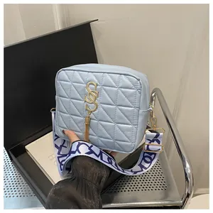 Detail of light blue quilted crossbody bag with golden logo, tassel, and printed strap
