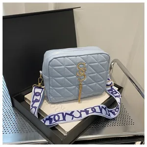 Detail of sky blue quilted crossbody bag with golden logo, tassel and wide strap