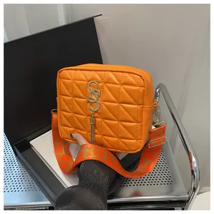 Close-up of quilted orange crossbody bag with gold metal logo and stylish tassel detail
