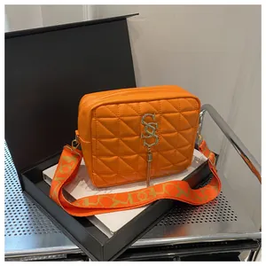 Detail of orange quilted crossbody bag featuring a golden S-logo and stylish wide strap