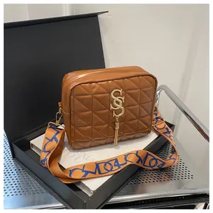 Detail of brown quilted camera bag with gold S-logo and wide jacquard shoulder strap
